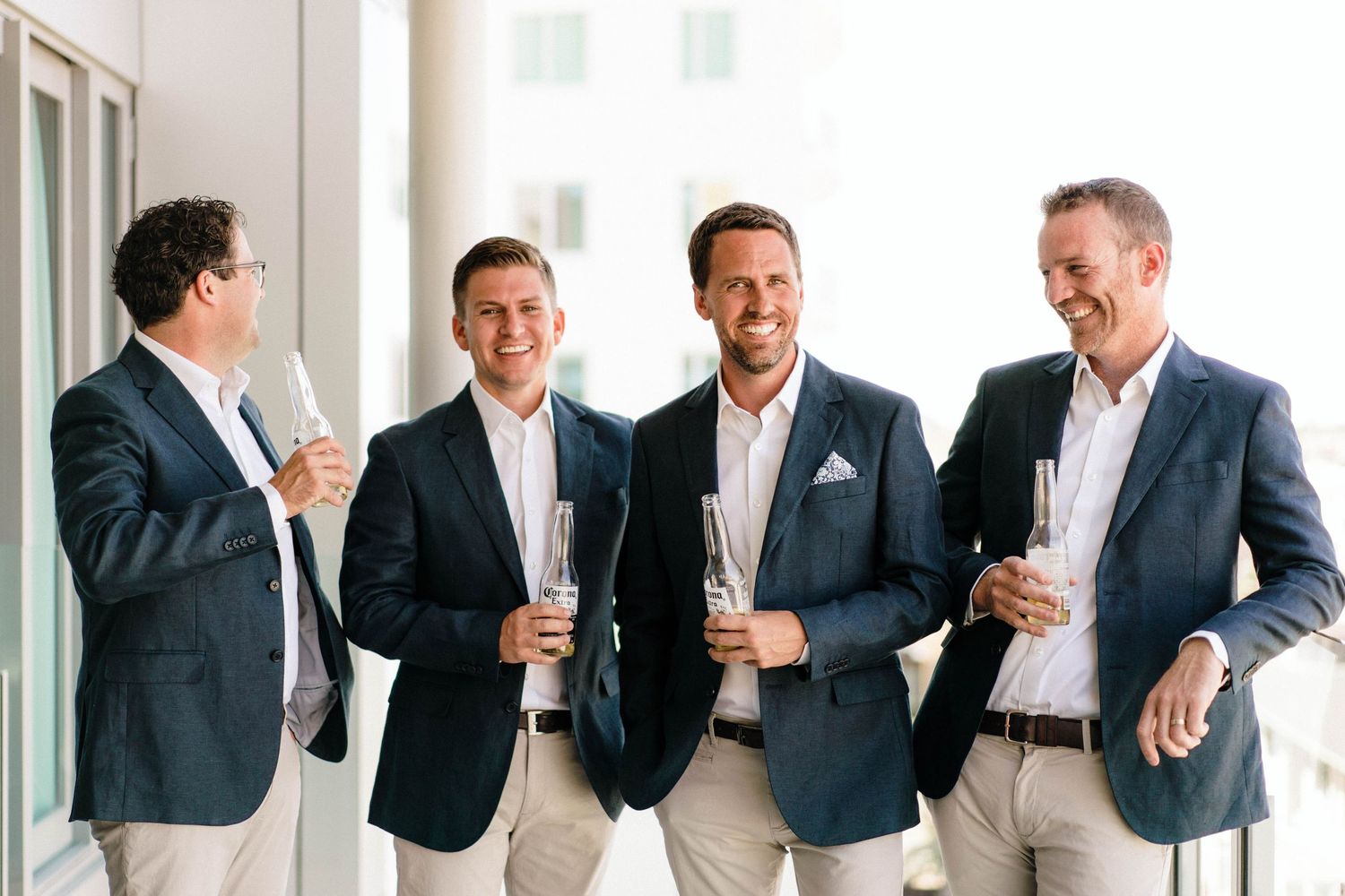 Four business professionals in blazers stand together having drinks and casual conversation at a networking event.