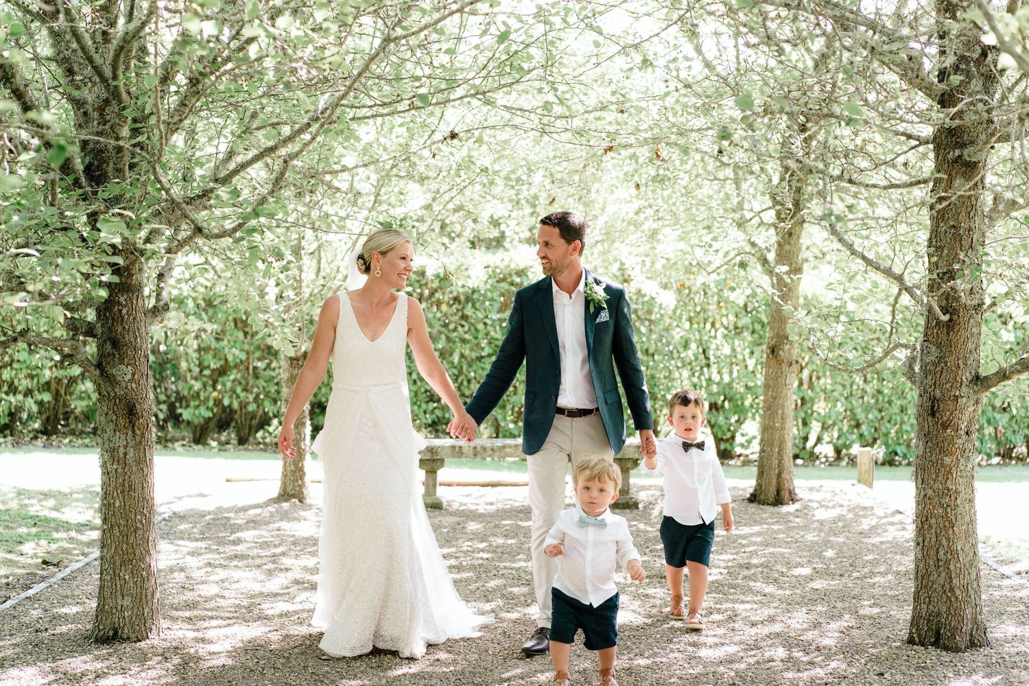 A couple and two small children walk hand in hand down a tree-lined path on their special day.