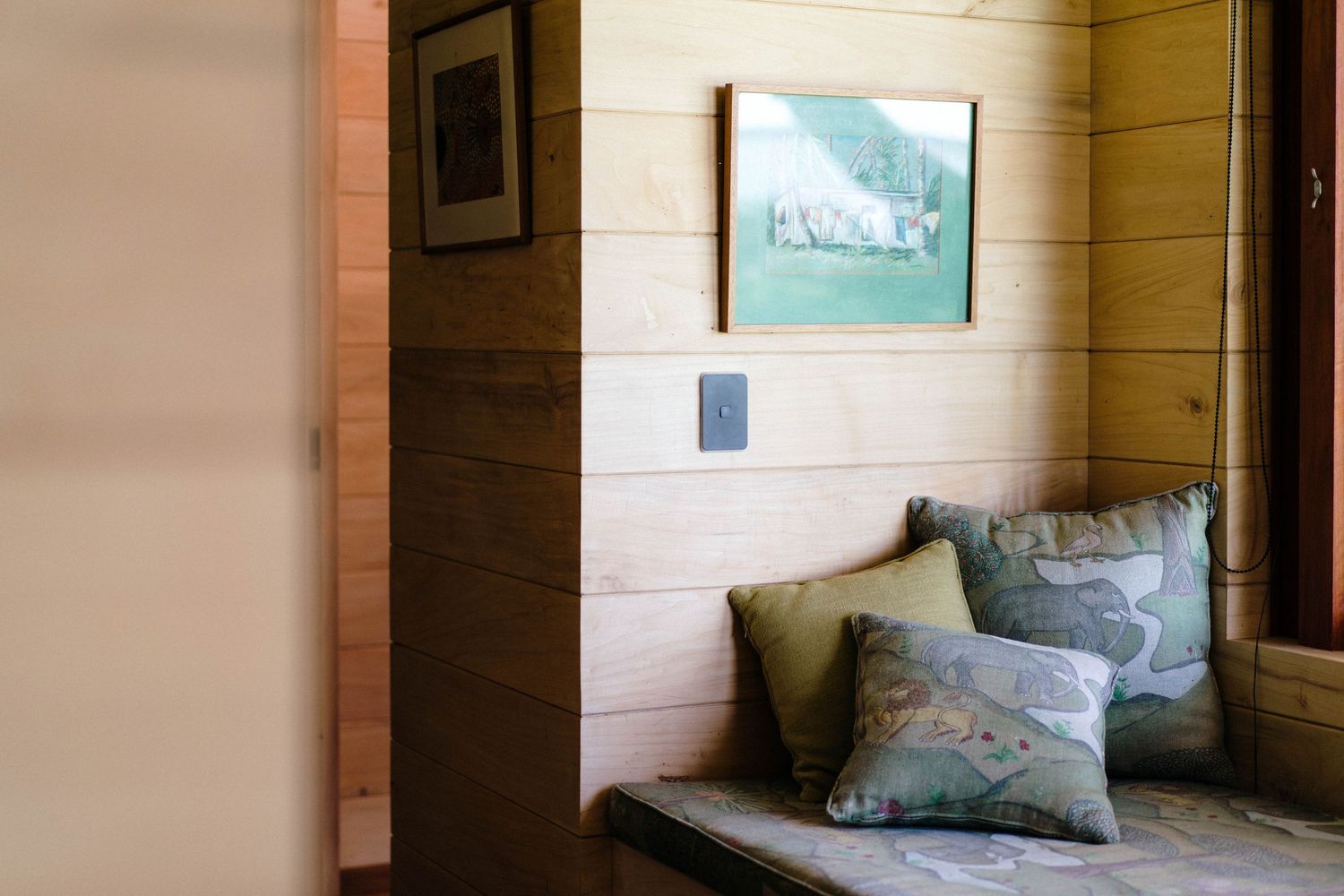 A cozy corner seating nook with decorative pillows and a framed landscape artwork on wooden paneled walls.