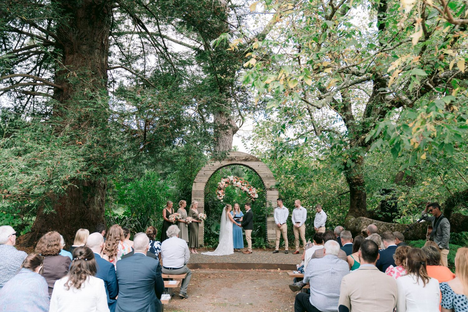 Wedding ceremony setup in a tranquil forest clearing with wooden benches arranged for guests.