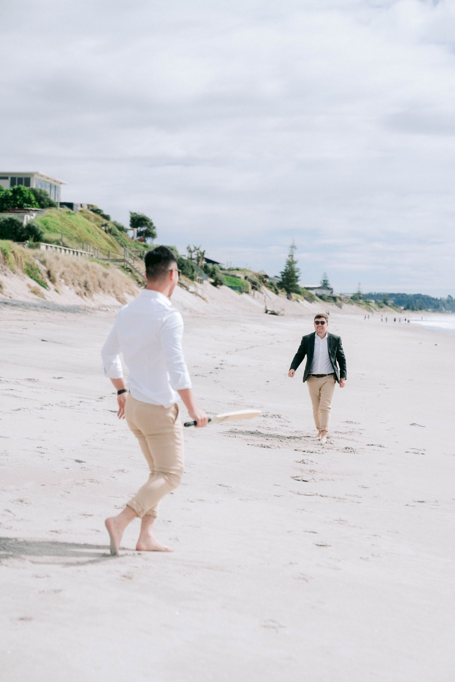 People in light colored clothing playing and walking along a scenic sandy beach on a cloudy day.