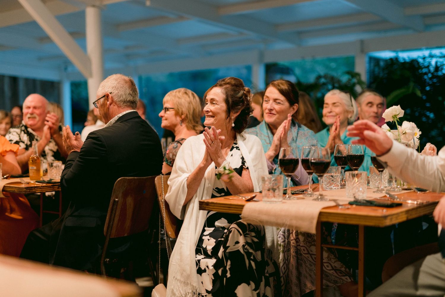 Wedding reception guests enjoying dinner and conversation under blue-tinted lighting.
