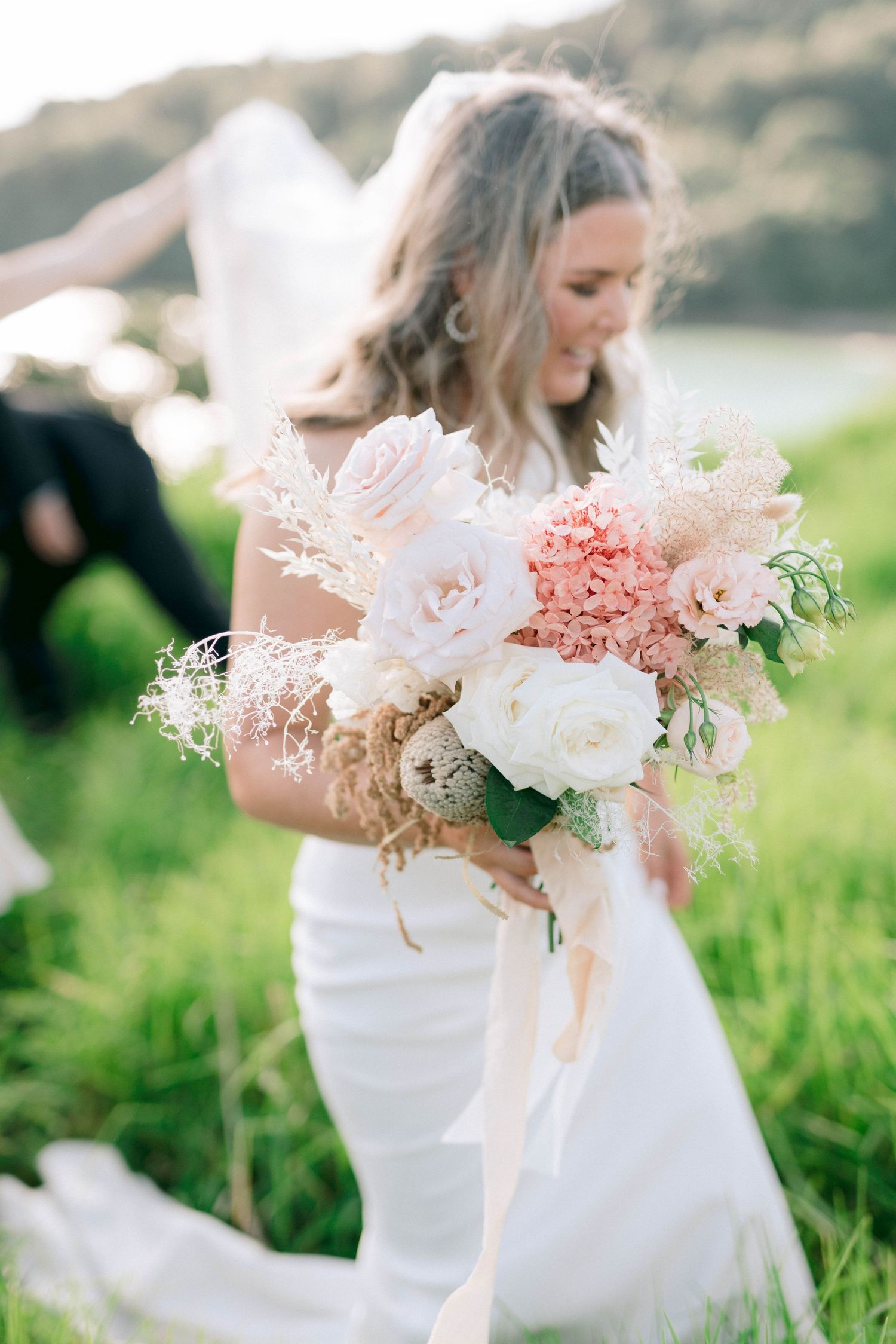 Elegant bridal bouquet with white and coral flowers against a flowing white dress.