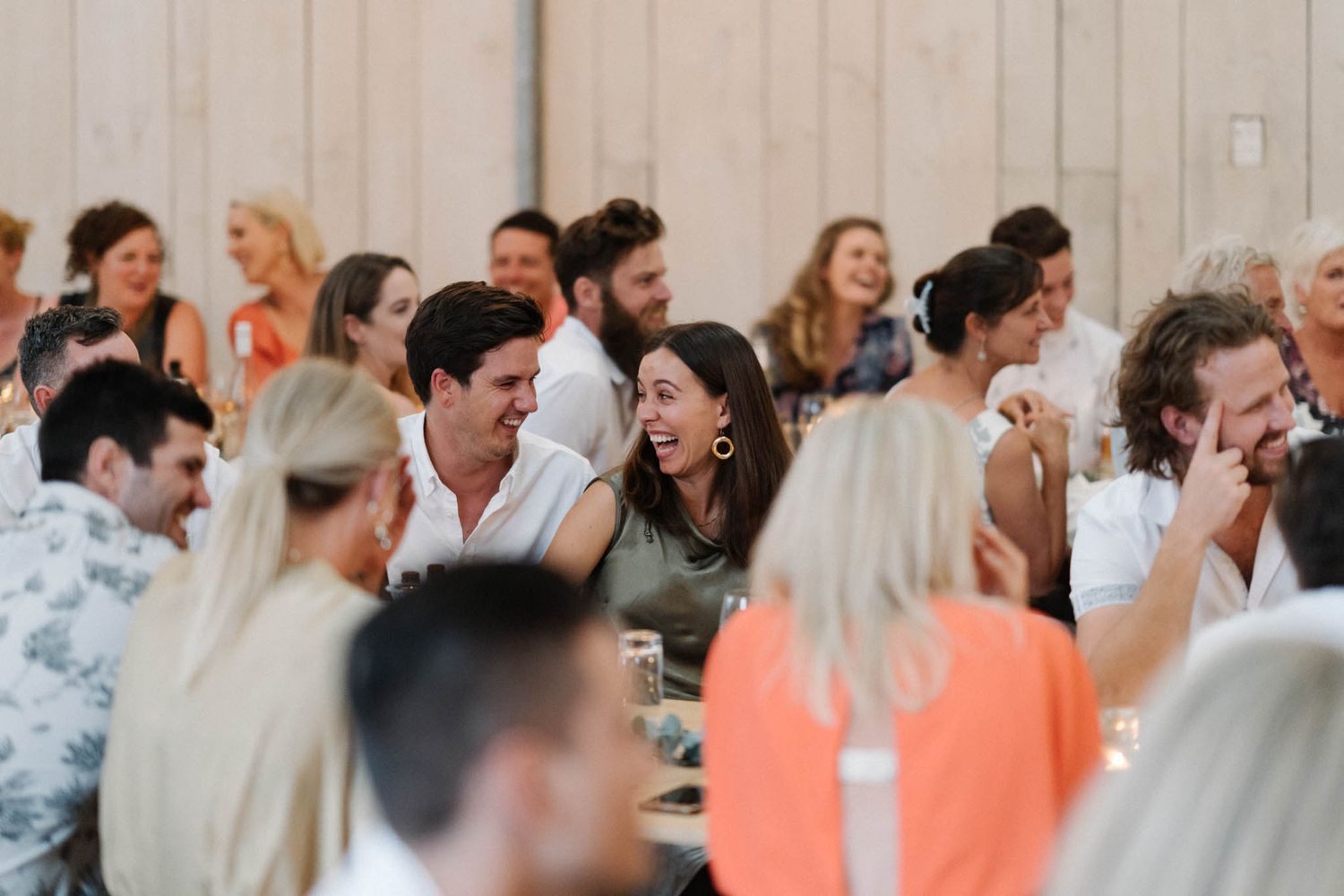A candid shot of wedding guests laughing and enjoying themselves at reception tables.