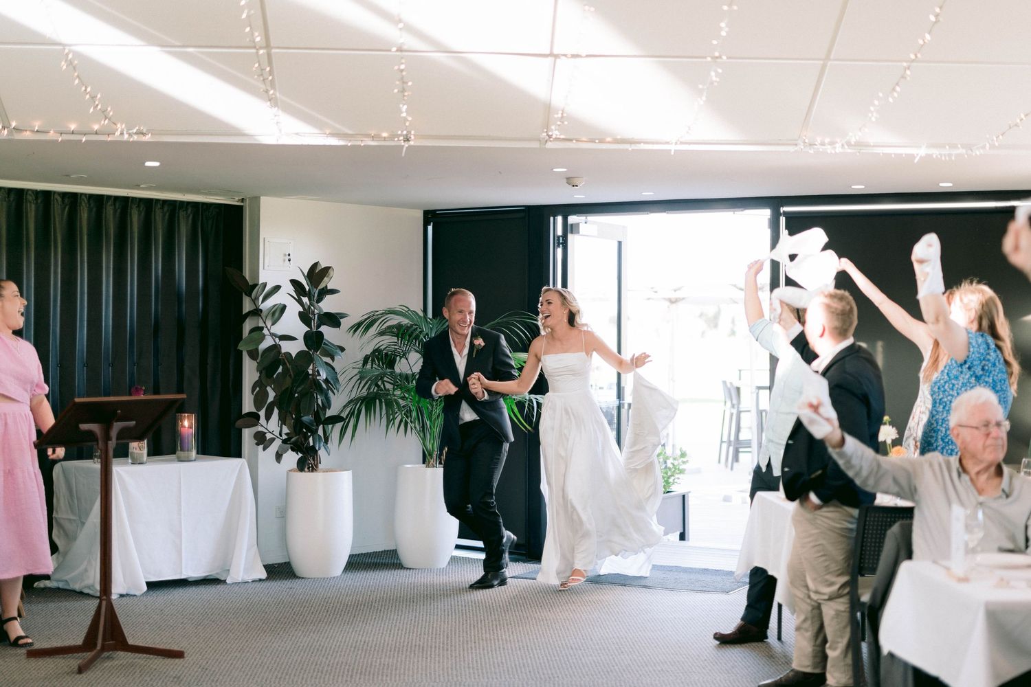 Wedding guests dance and celebrate in a bright modern indoor reception venue.