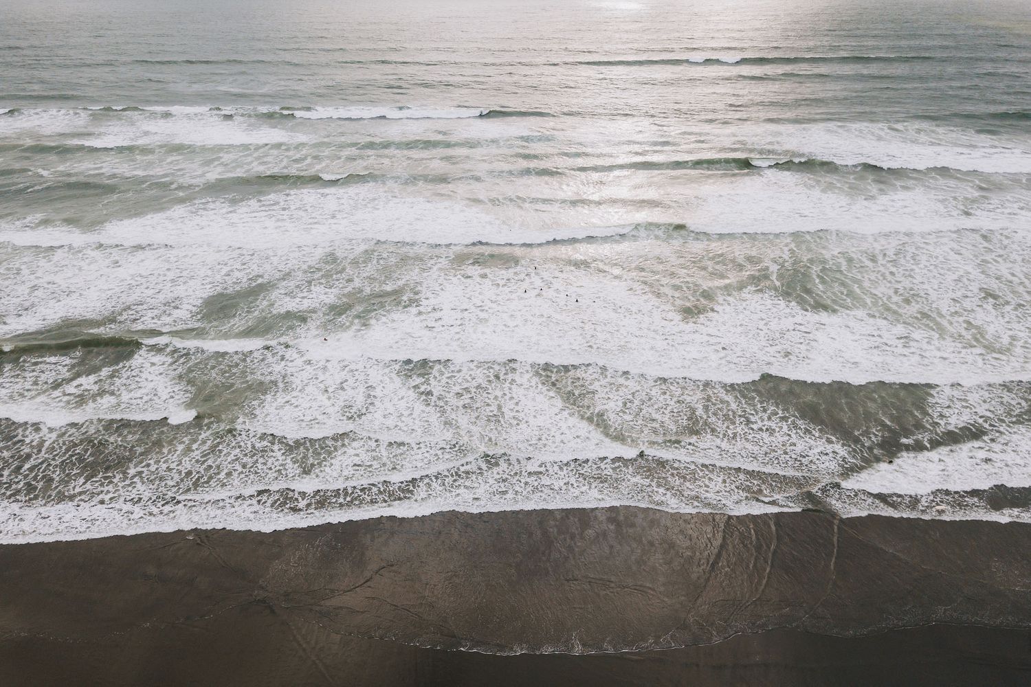 Aerial view of ocean waves crashing onto a sandy beach with white foam patterns forming along the shoreline.