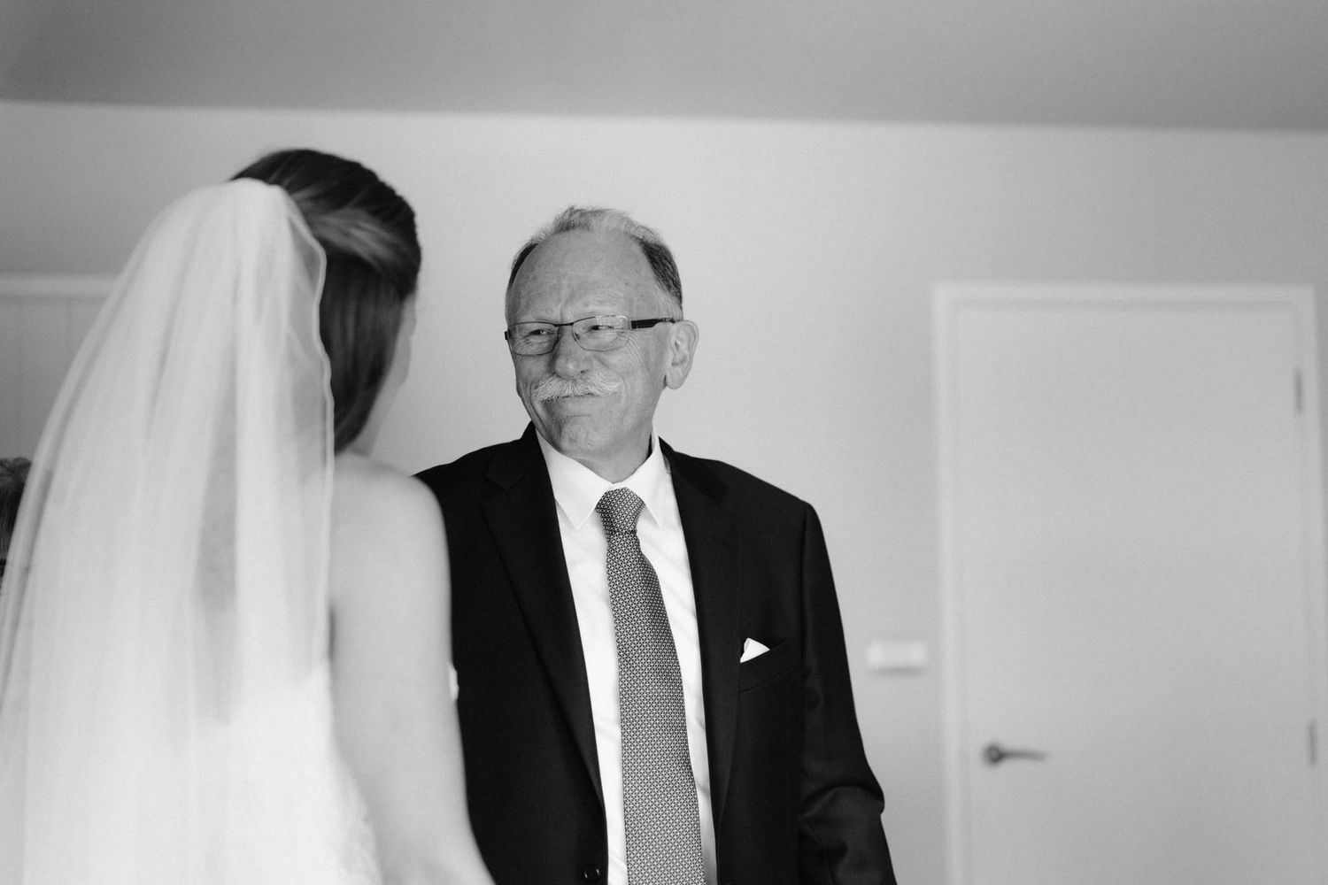 Black and white photograph showing emotional moment between a bride in her veil and an older man in a suit and tie.