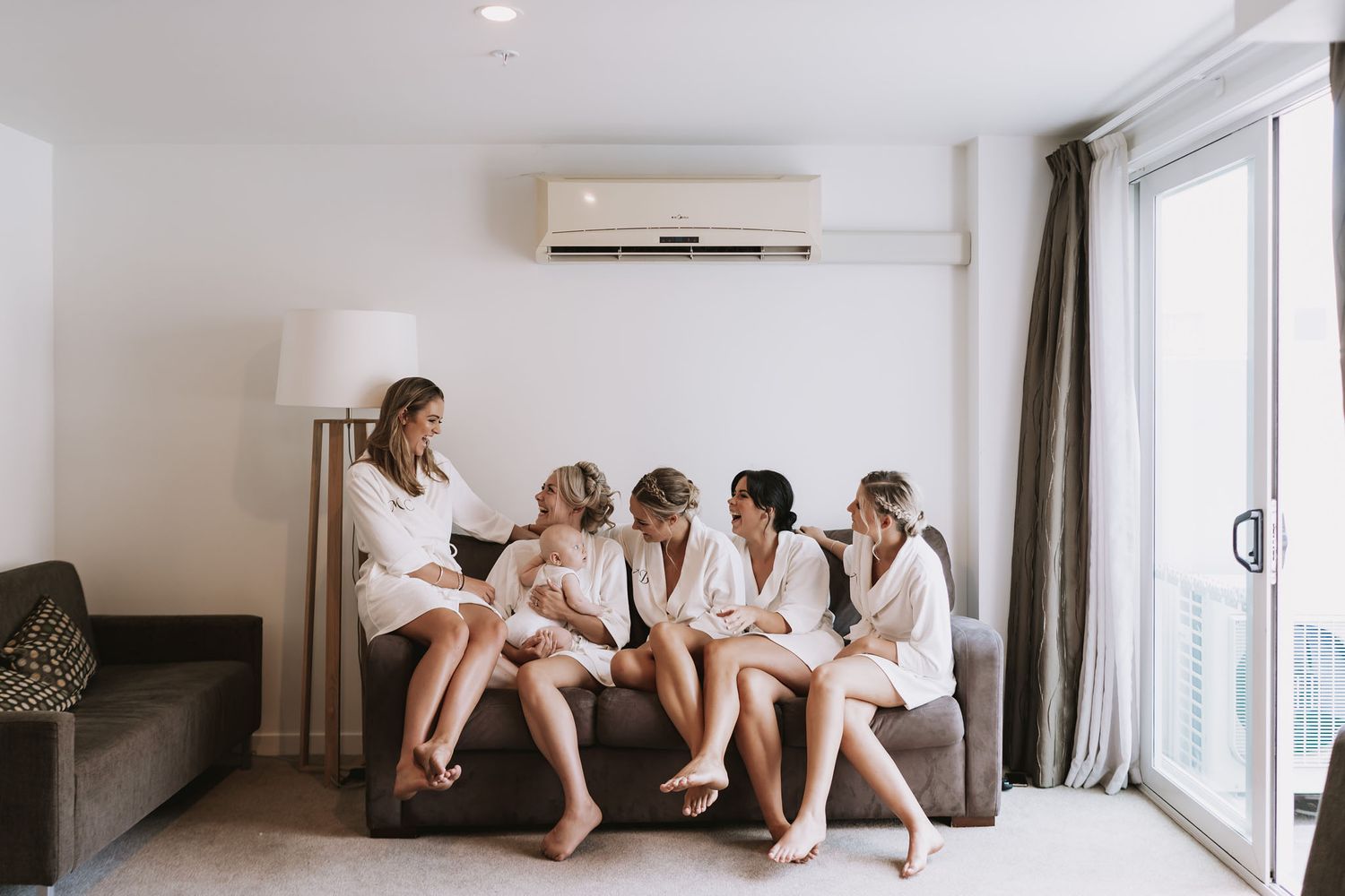 People wearing white robes sit in various relaxed poses along a minimalist white room with natural lighting.