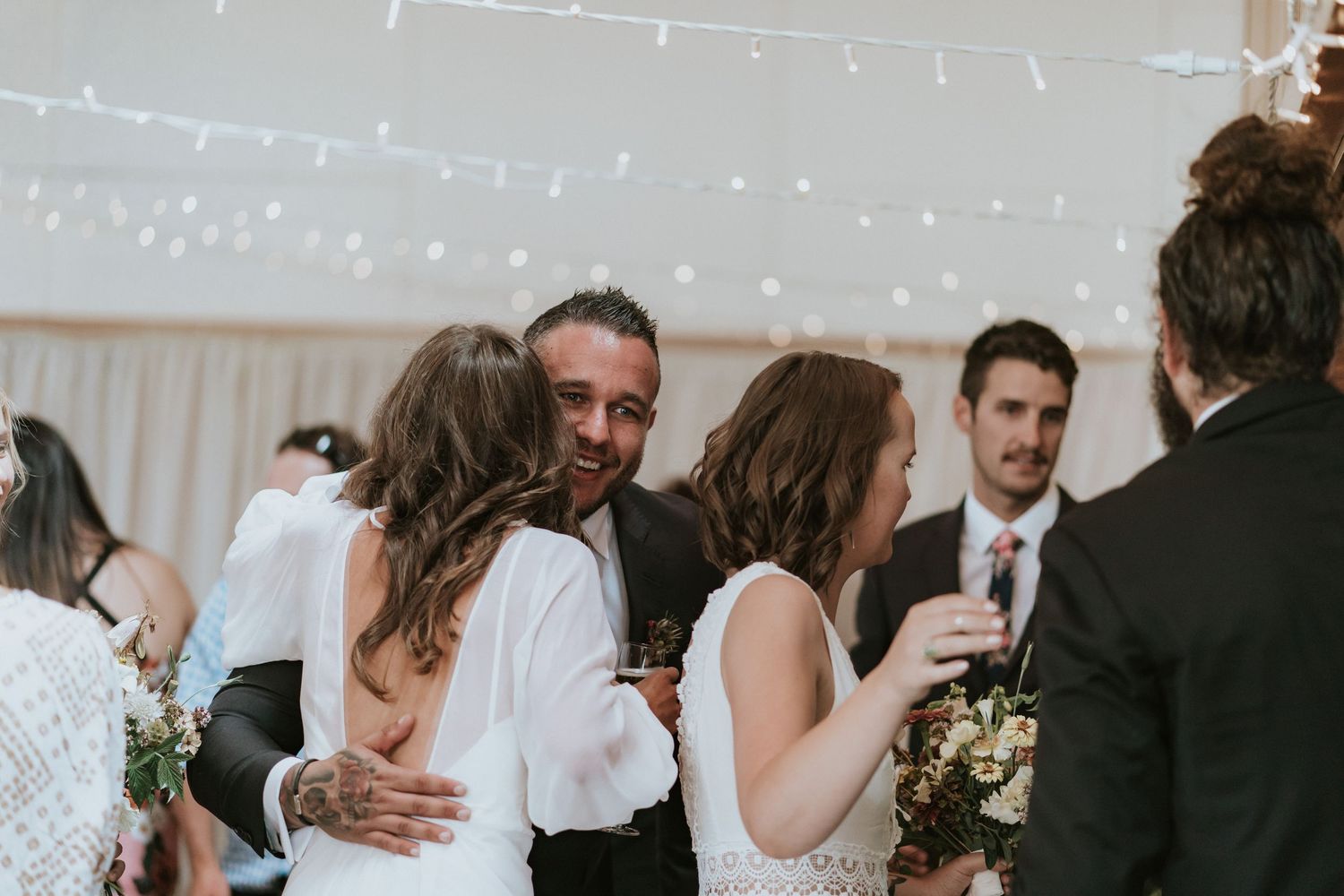 Wedding guests share heartfelt embraces and conversations during a celebration reception at an indoor venue.