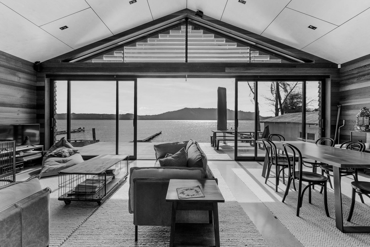 Modern black and white interior of a lakeside home with large windows overlooking mountains and water.