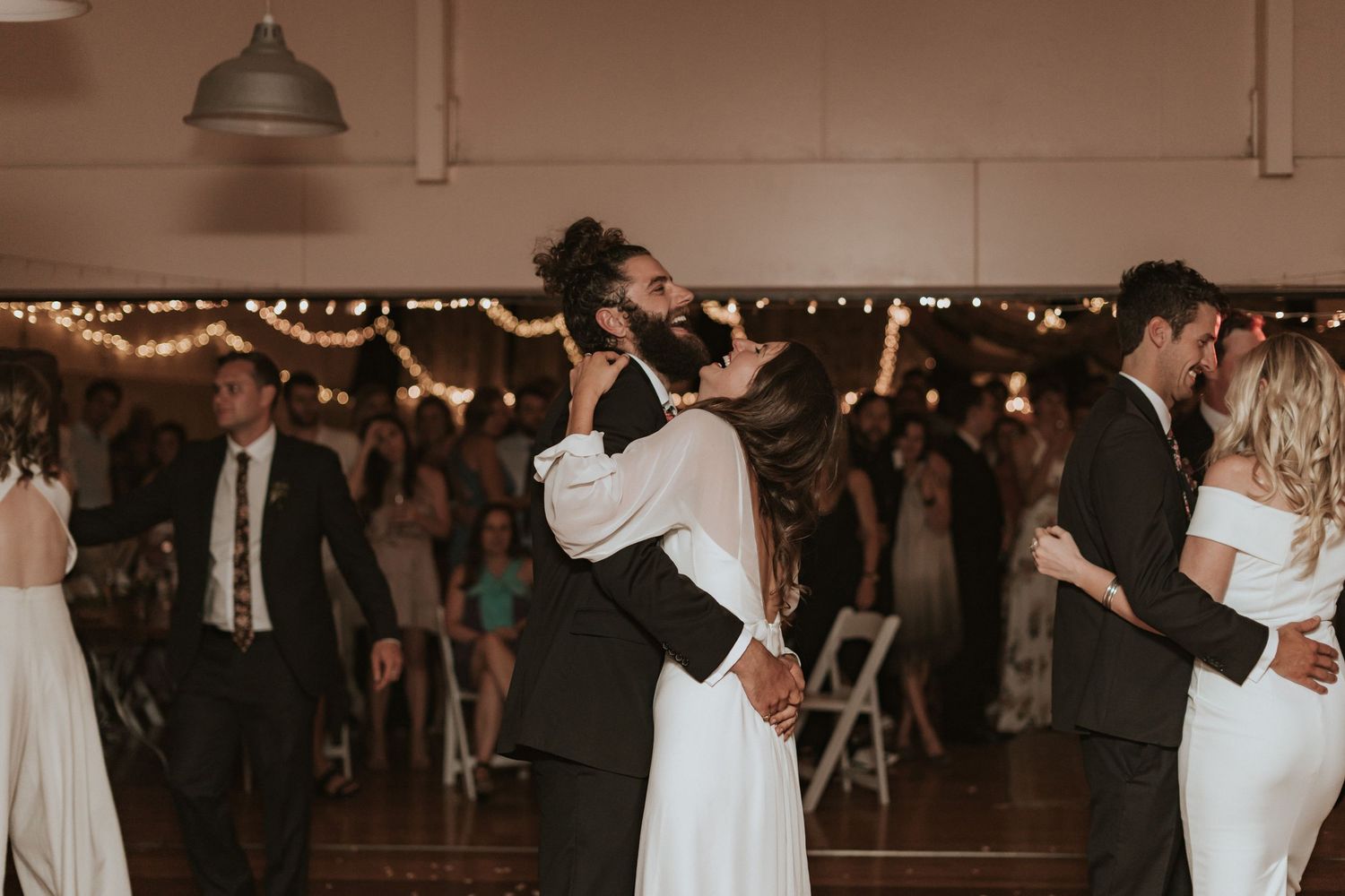 Couples dance together at an elegant reception venue with dim lighting and romantic twinkle lights overhead.