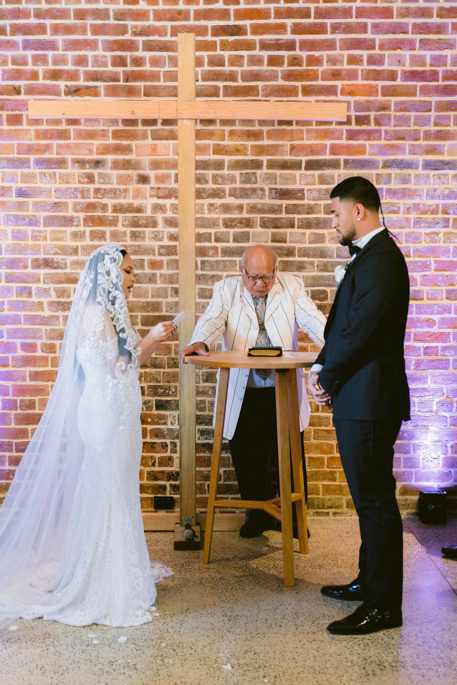 A first look moment unfolds between a couple against an exposed brick wall in an industrial venue.