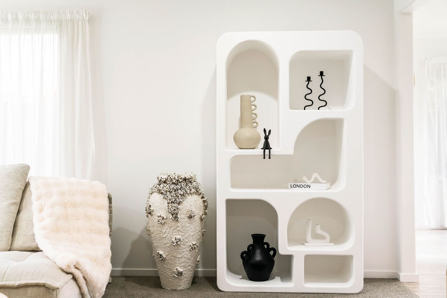 Modern white built-in shelving unit with curved edges displaying decorative vases and objects in a minimalist living room.