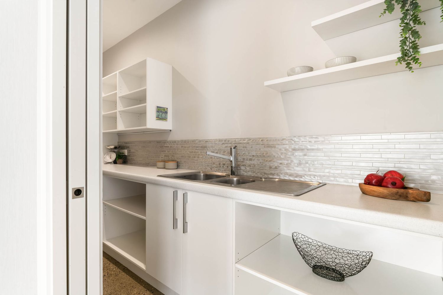 Modern white kitchen with floating shelves, subway tile backsplash, granite countertops, and decorative plants.