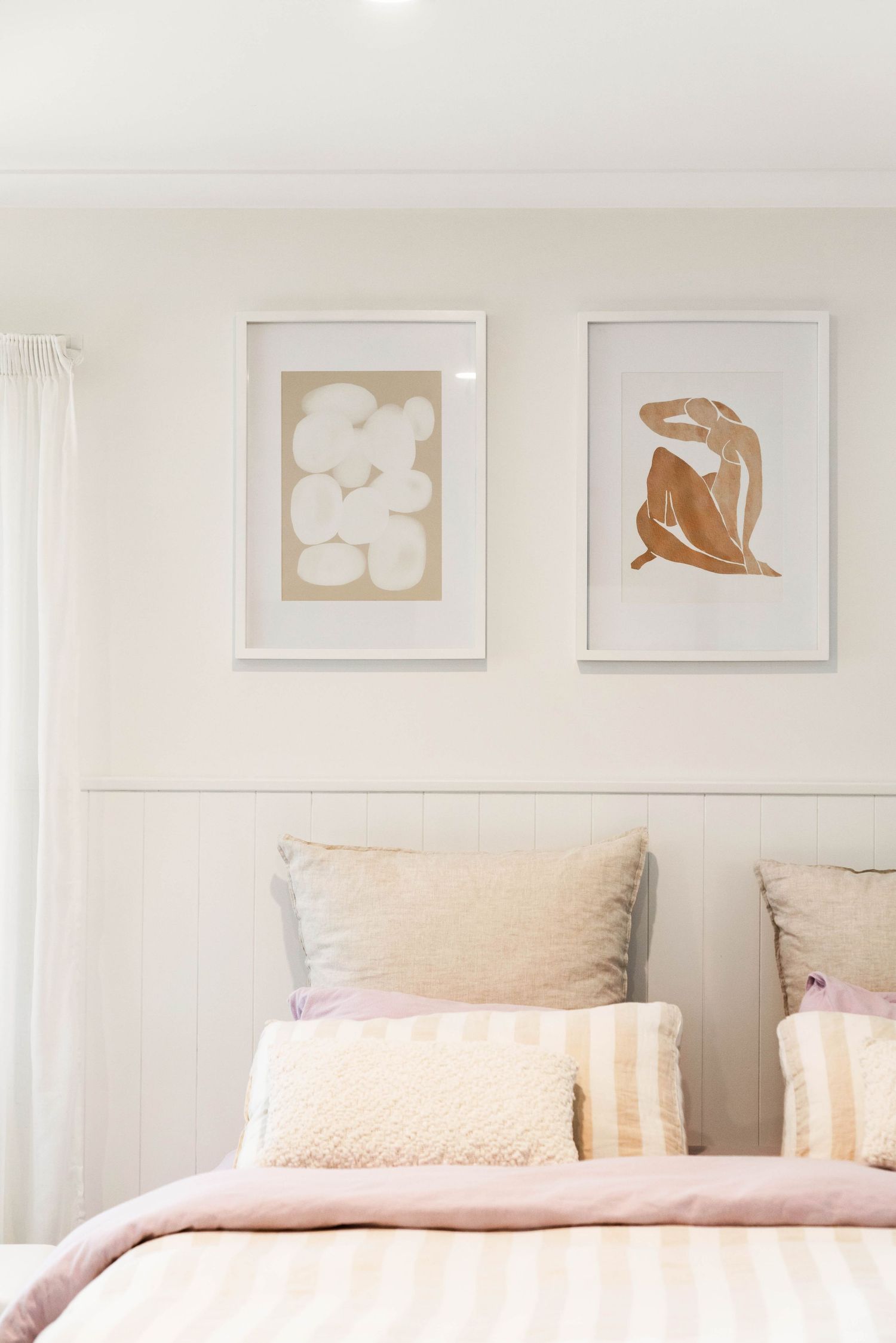 Minimalist bedroom interior with pink bedding and neutral beige artwork arranged in a row on white walls above the bed.