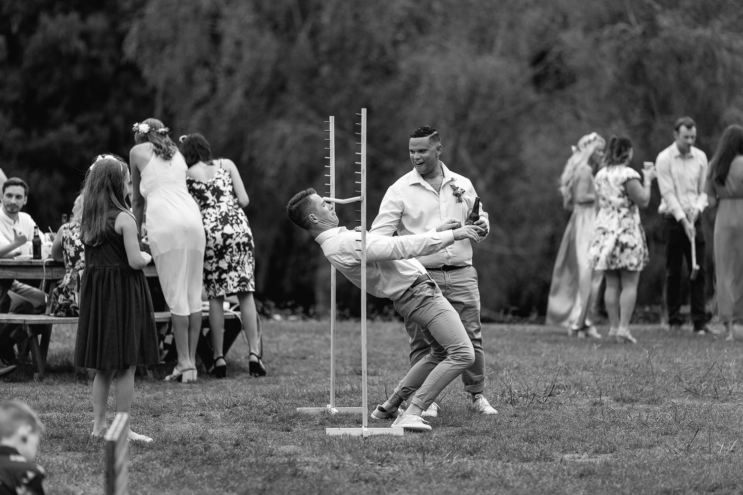 A person playing limbo at an outdoor gathering while onlookers watch in black and white photography.