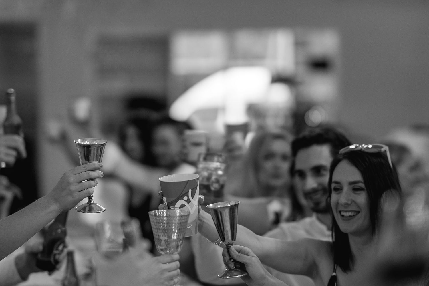 People raise their glasses in a celebratory toast at a social gathering captured in black and white.