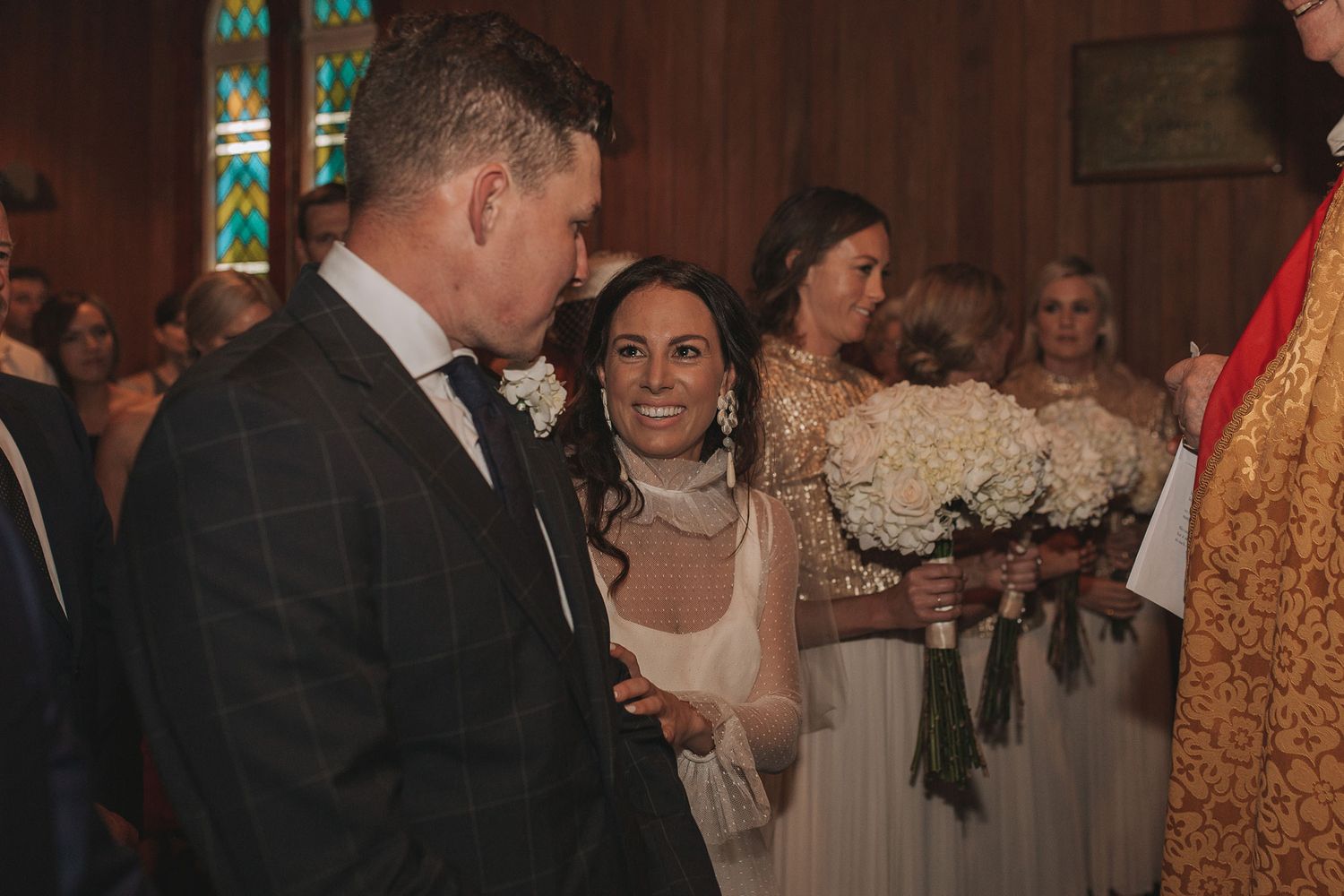 Wedding reception crowd mingling in a warmly lit venue with golden decor and formal attire.