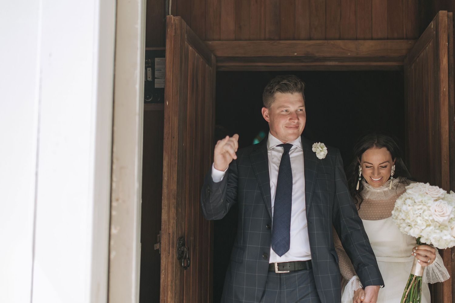 Wedding photo showing couple exiting wooden church doors after ceremony.