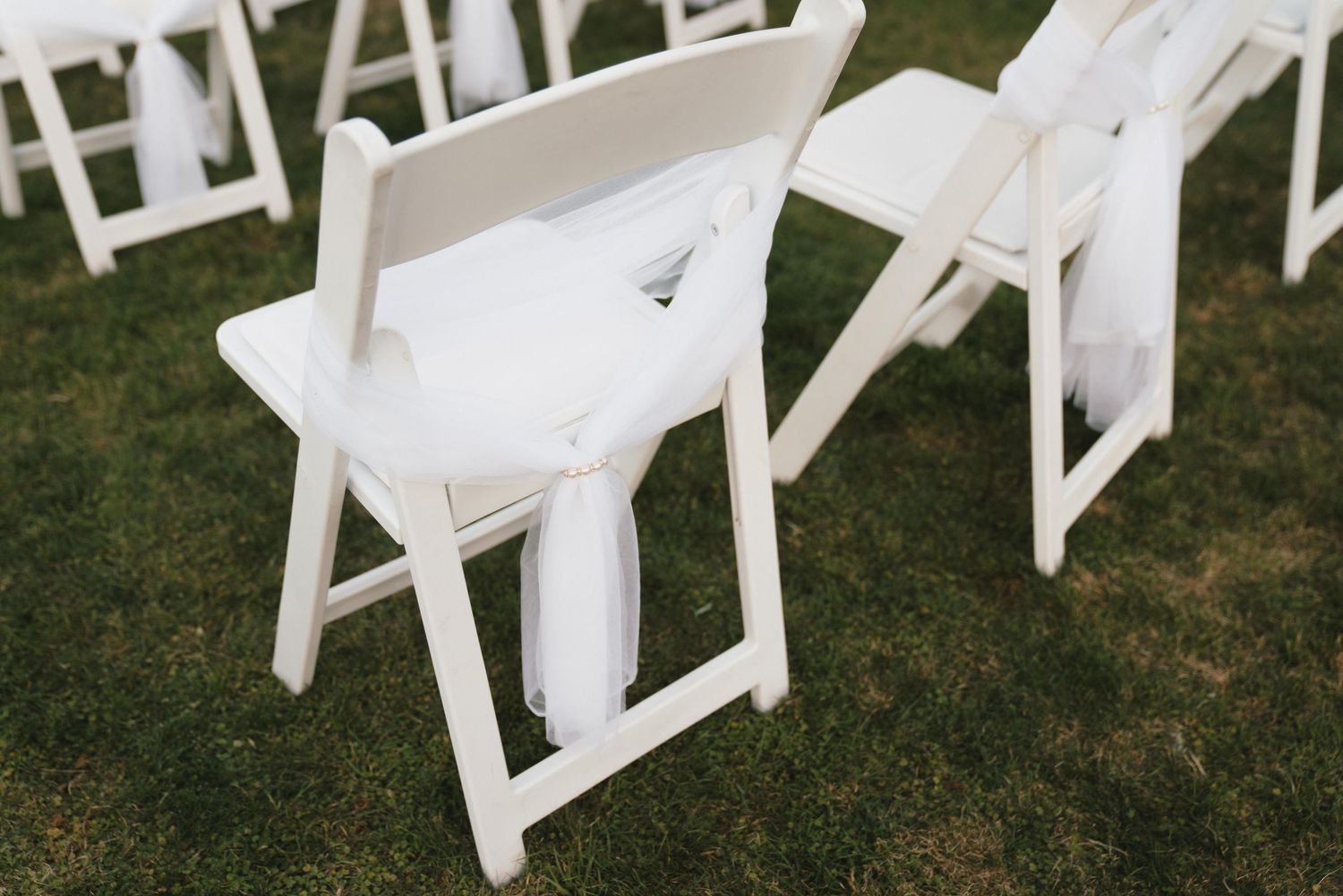 White folding chairs arranged in rows on a lush green lawn for an outdoor wedding ceremony.