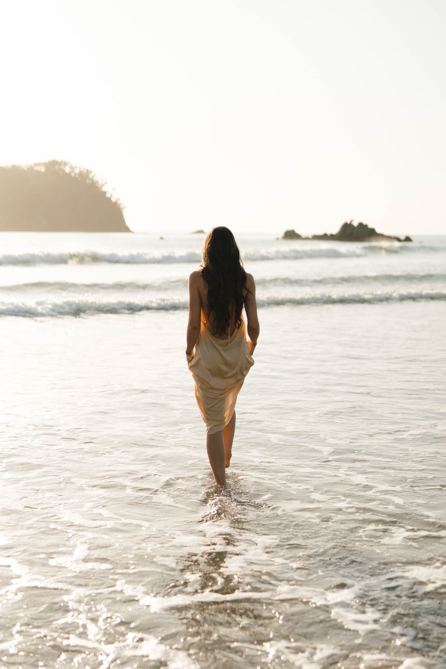 A serene sequence of someone walking through gentle ocean waves at sunset with a white flowy dress.