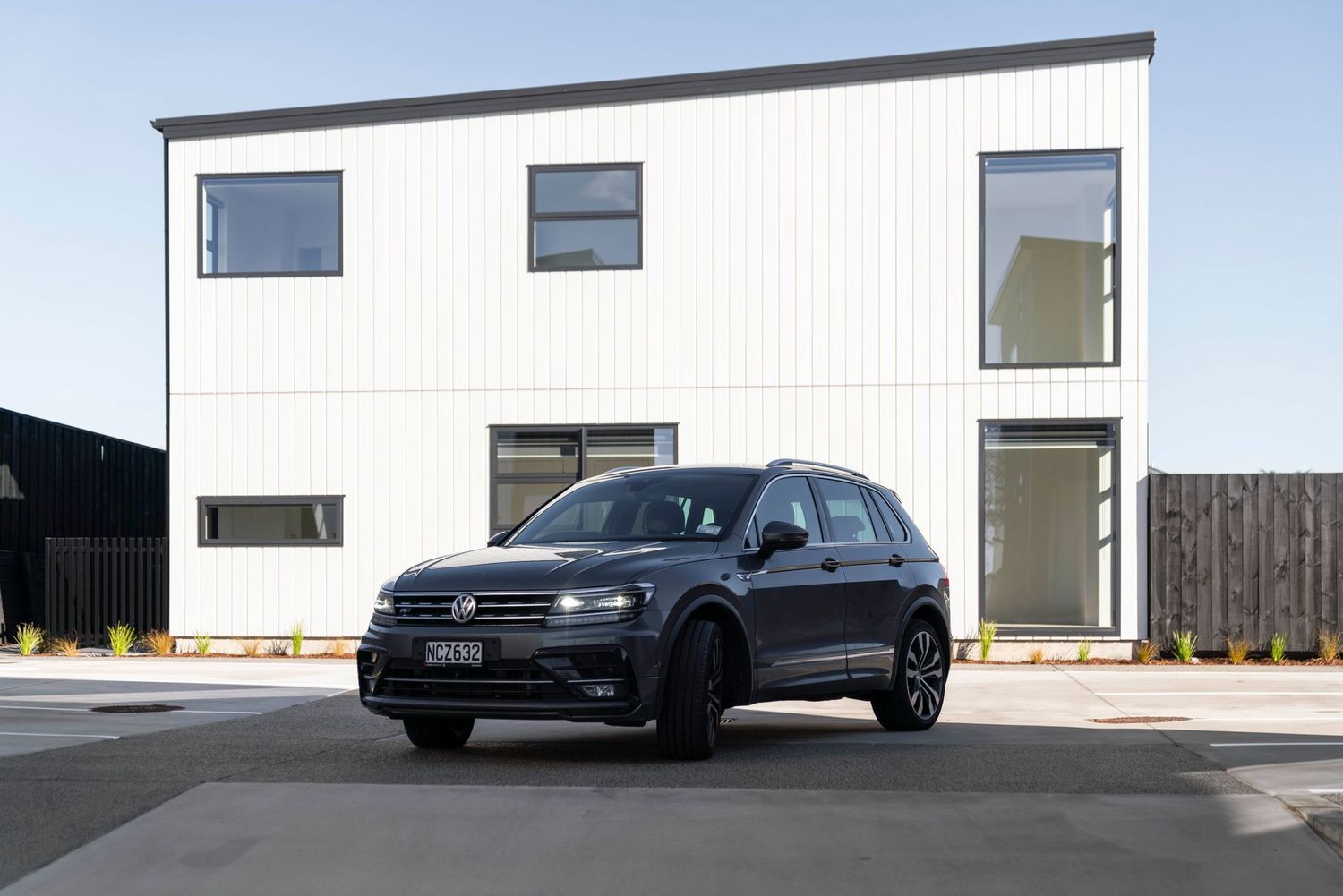 Modern black Volkswagen SUV parked in front of white contemporary house with minimalist design.