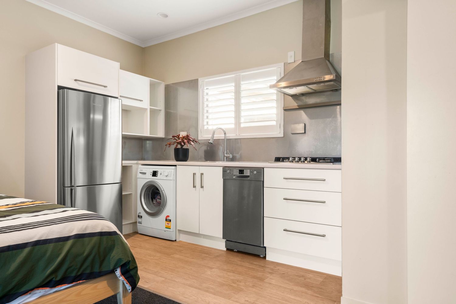 Clean white kitchen with stainless appliances and wooden flooring in compact layout.