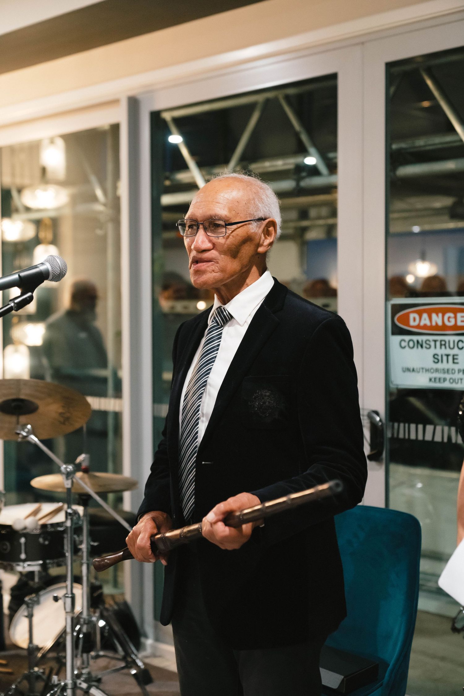 Speaker holding drumsticks on stage during a formal presentation.