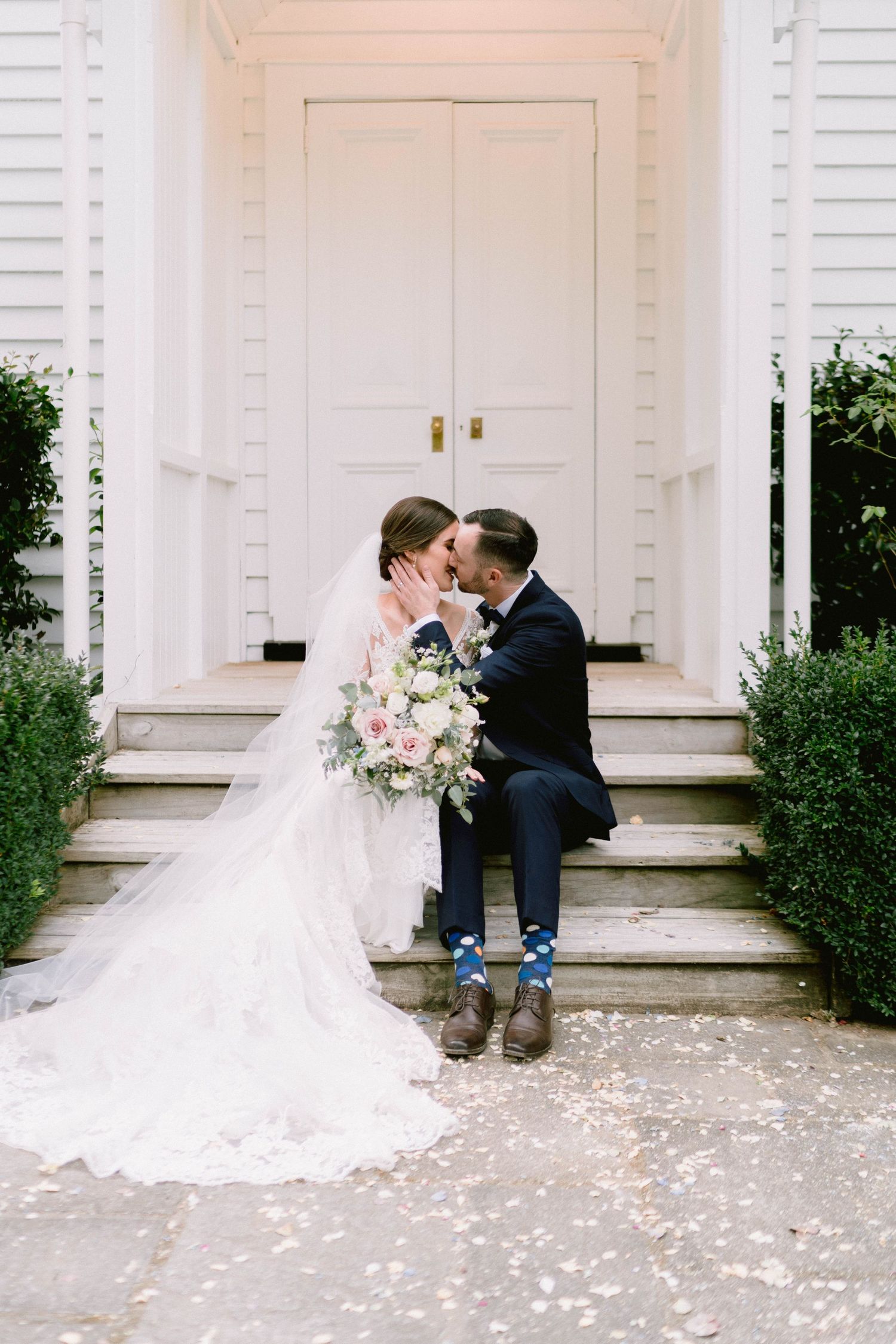 Romantic wedding portraits on white church steps scattered with flower petals.