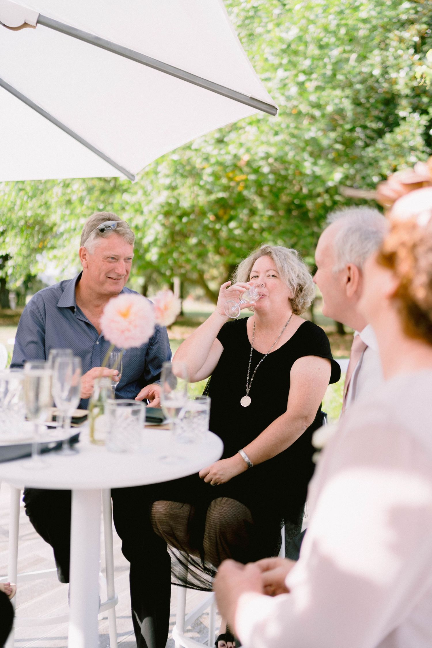 Wedding guests enjoying outdoor dining under a white umbrella.
