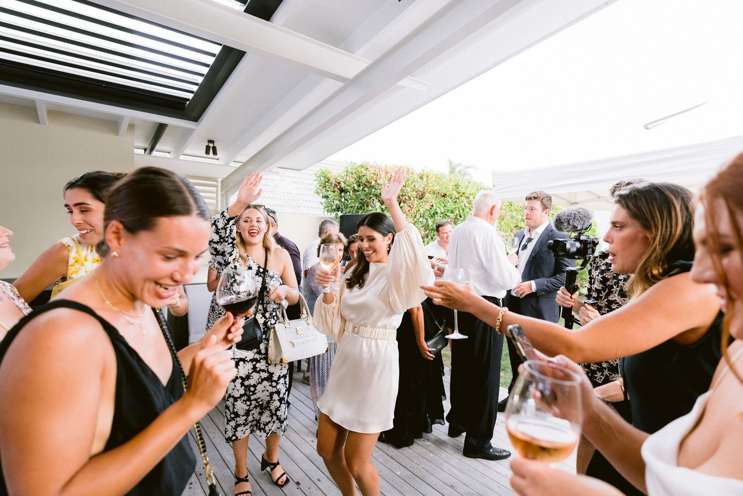 Wedding guests celebrate and dance at an outdoor reception on a covered deck.