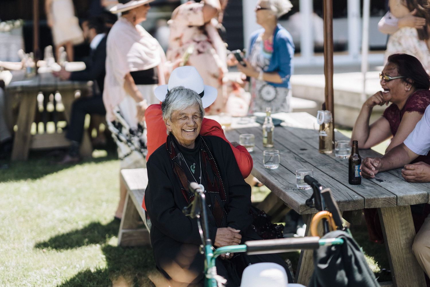 Senior guest with mobility scooter sits at outdoor picnic table during daytime event.