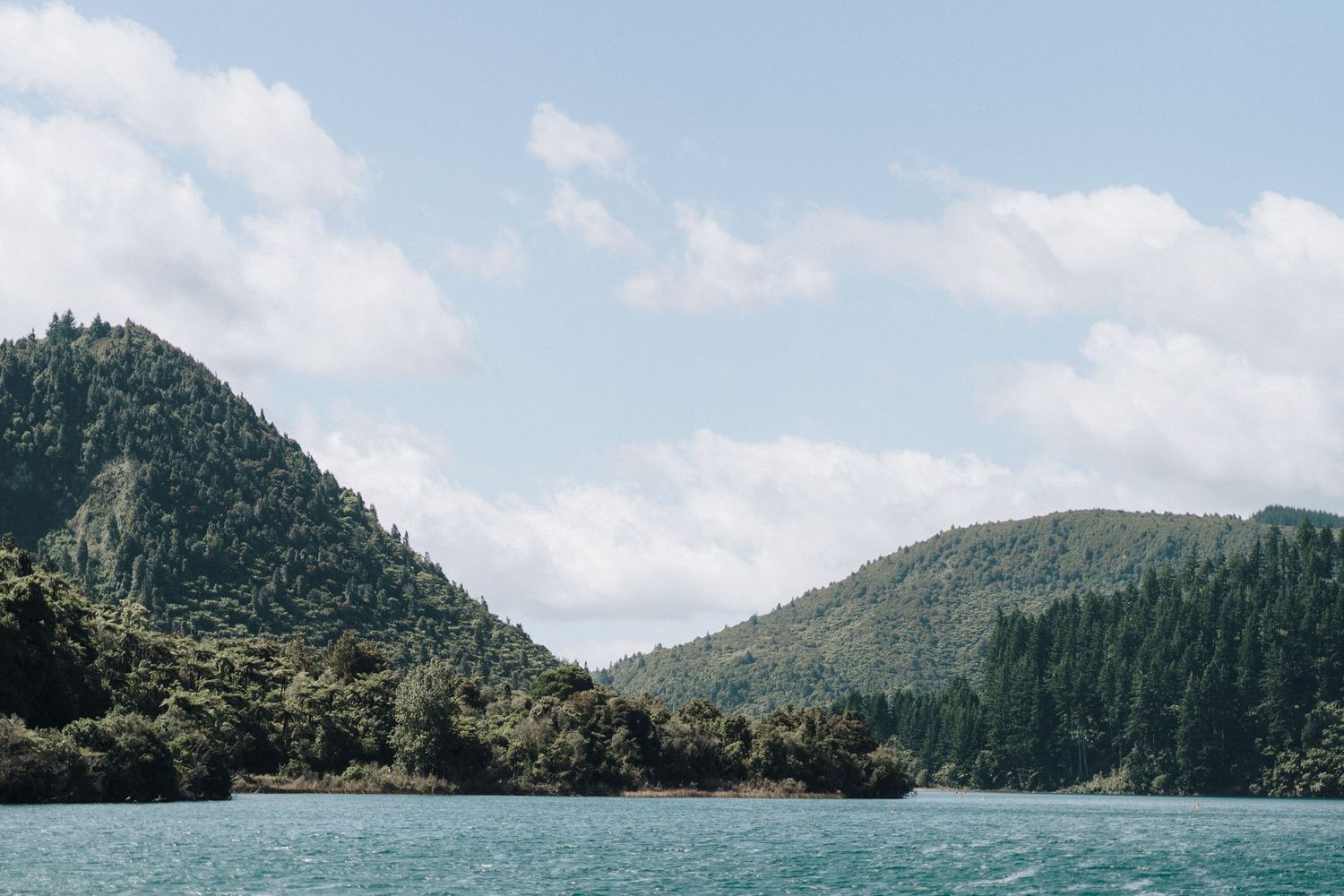 A panoramic view shows a series of green mountainous islands rising from calm waters under a blue sky.