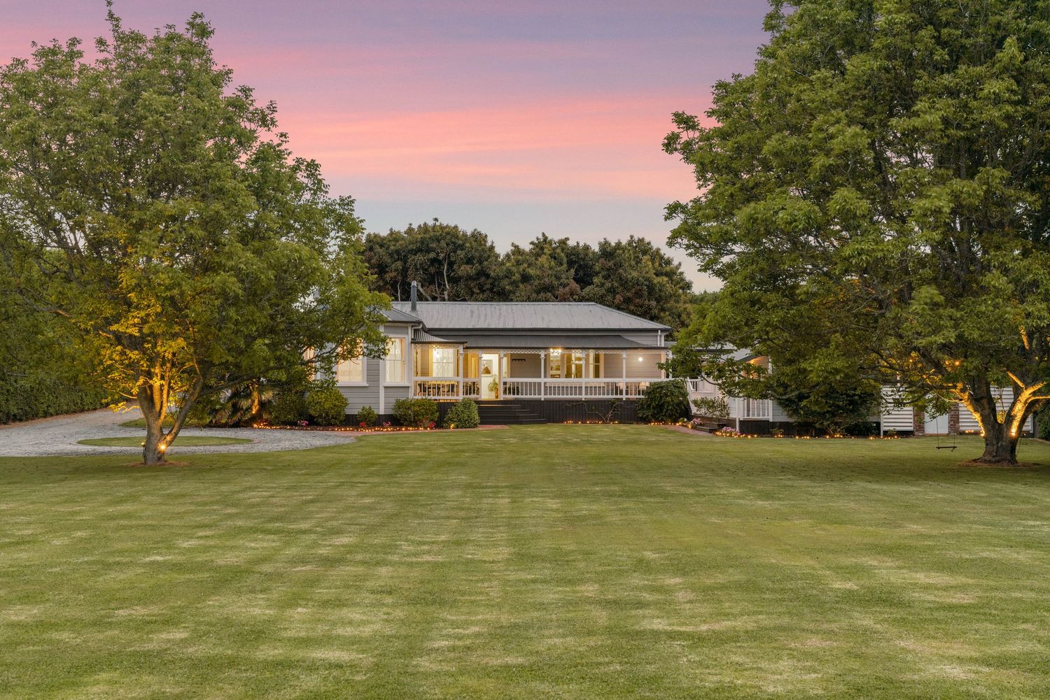 Ranch style home on spacious manicured lawn at dusk with pink sky and mature trees framing the property.