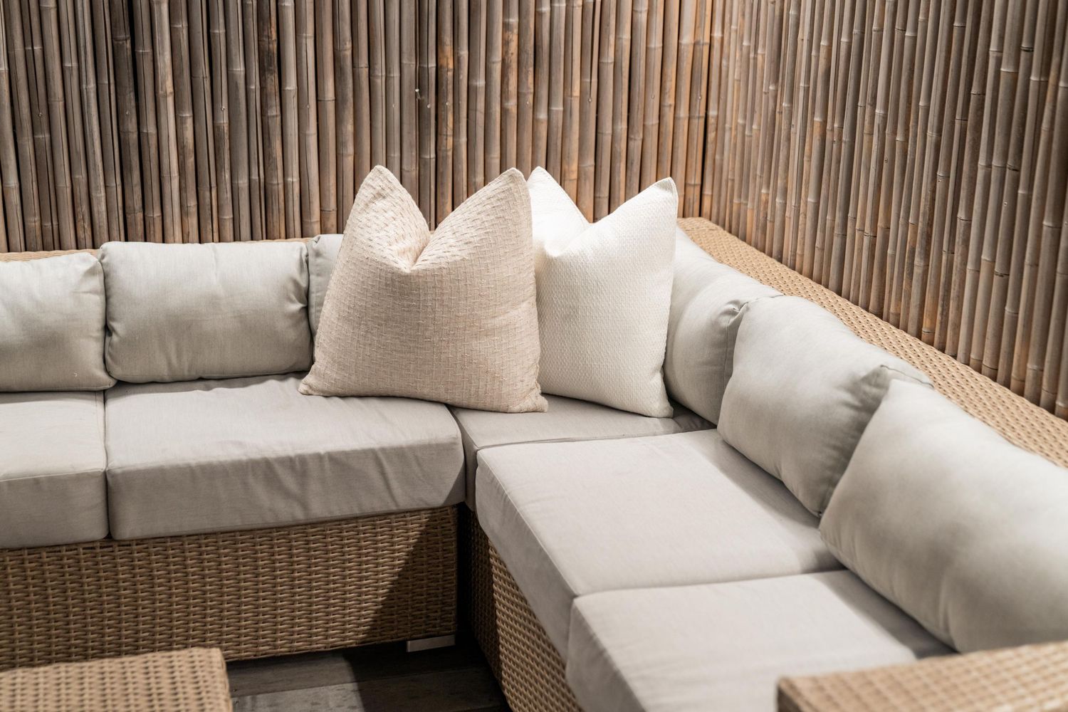 Contemporary outdoor lounge area with grey sectional sofa against bamboo screening.