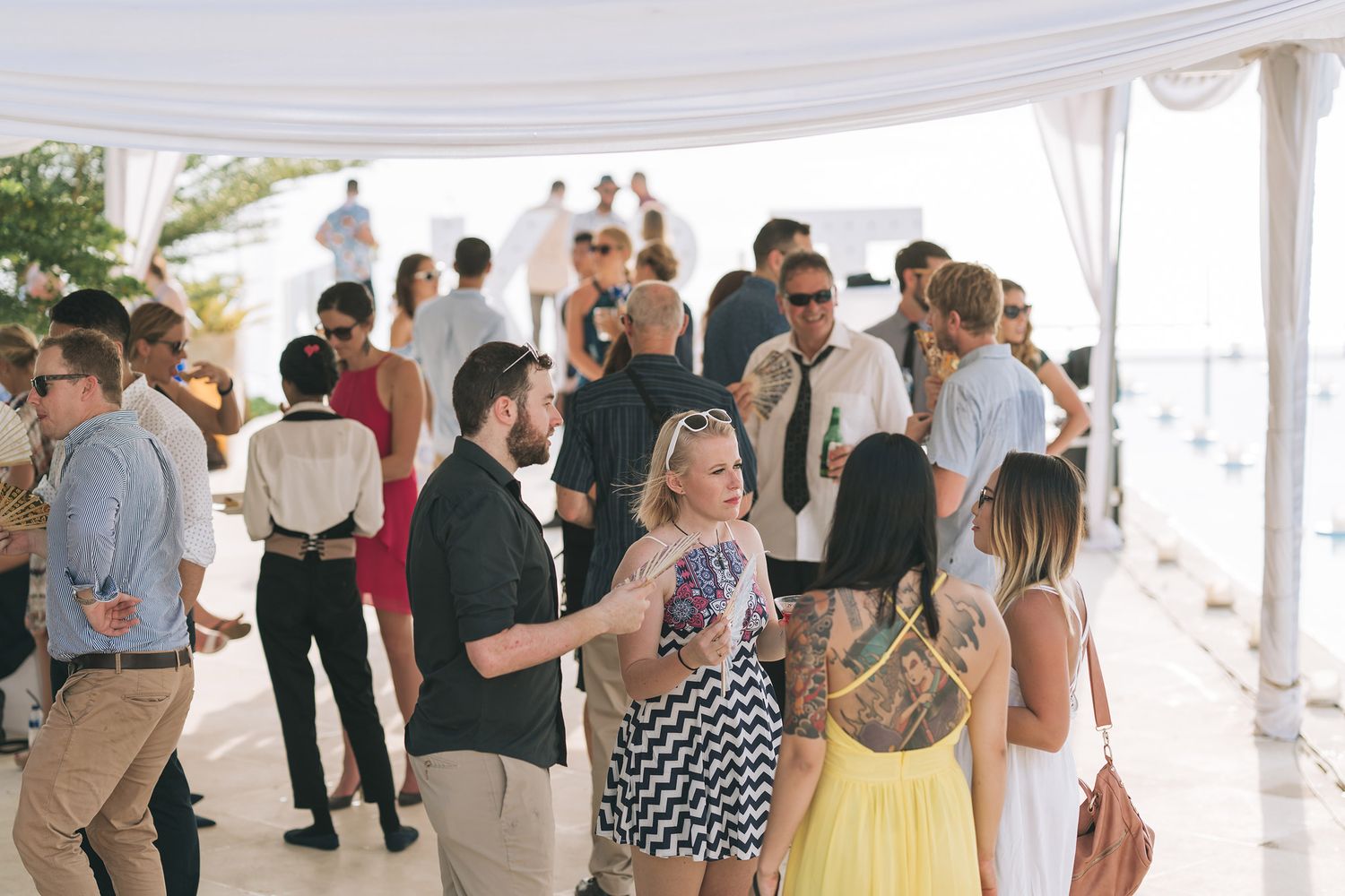 Wedding guests mingling and socializing under elegant white tent during reception.
