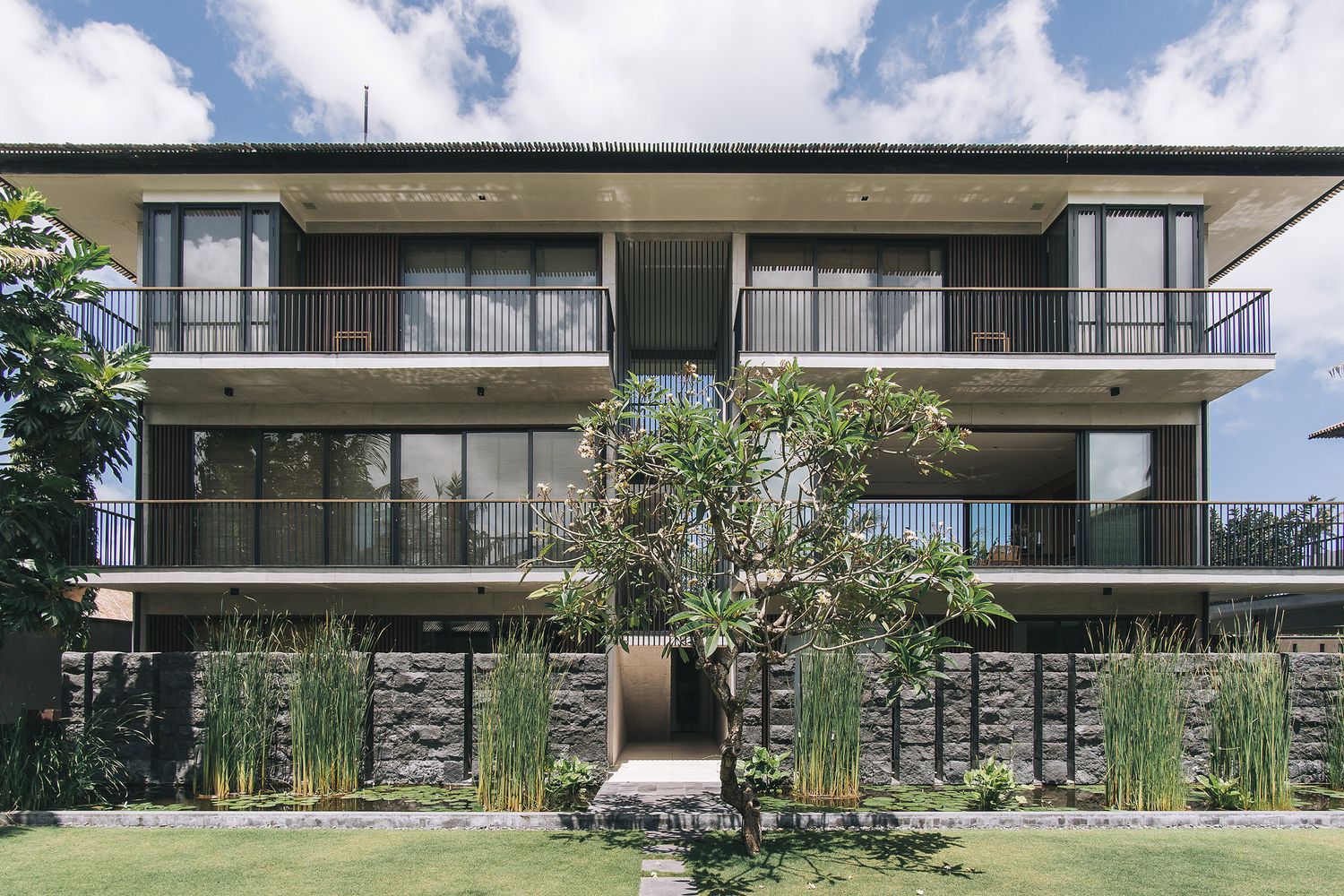 Modern three-story apartment building with stone facade and private balconies surrounded by landscaped gardens.