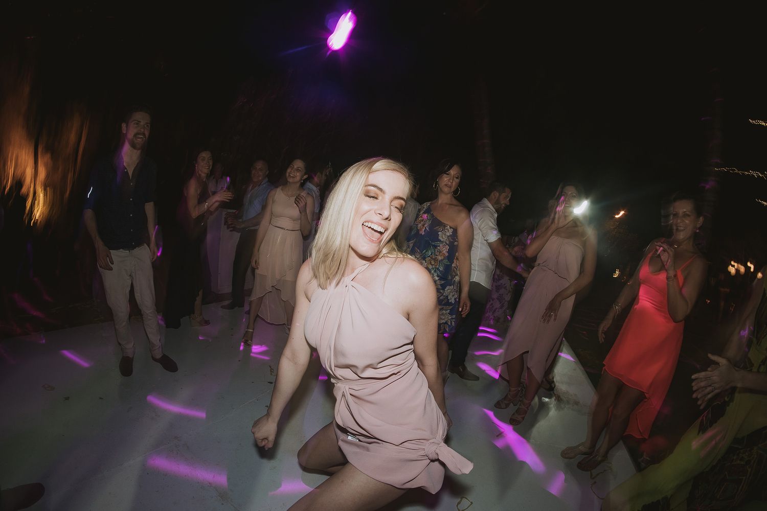 People dancing and enjoying themselves under purple lighting at a nightclub or party venue.