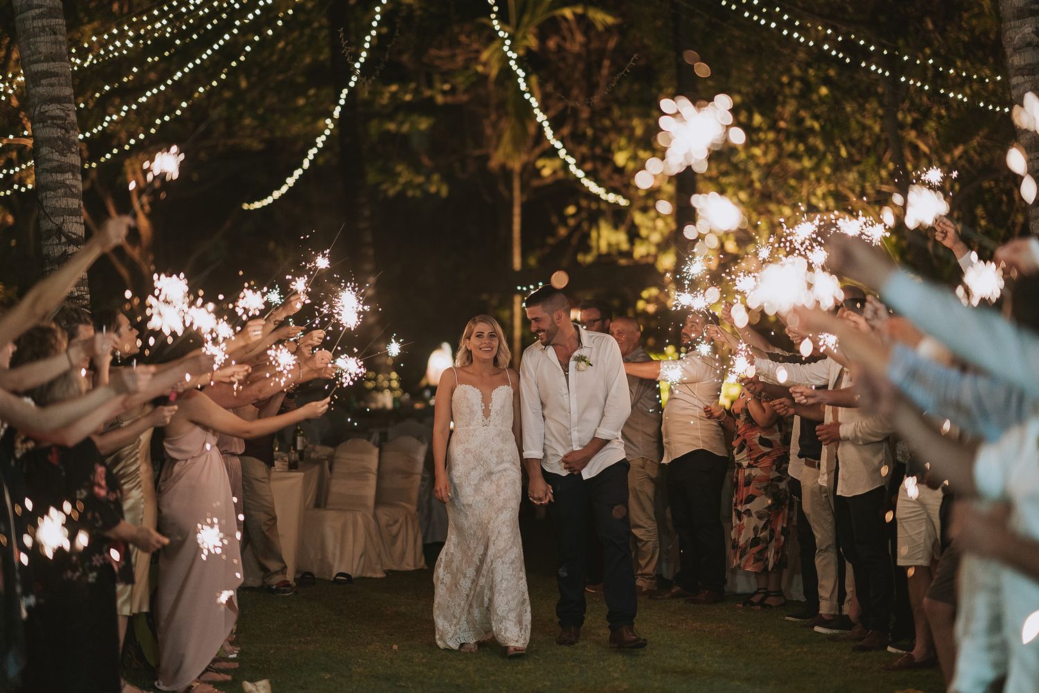 Wedding sparkler exit with guests creating illuminated pathway for couple.