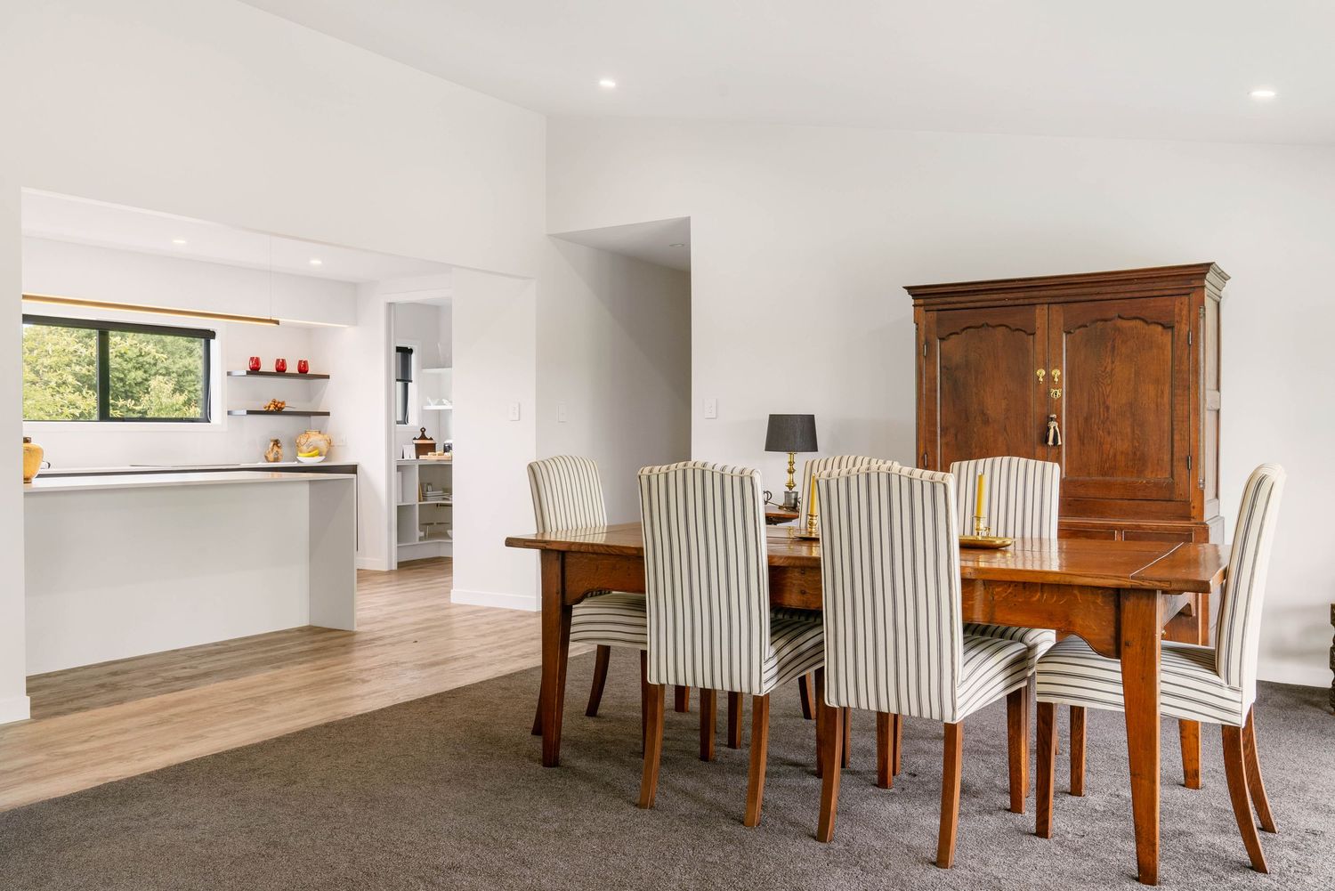 Contemporary open plan living space features white walls, hardwood floors, and traditional wood furniture with ample natural lighting.