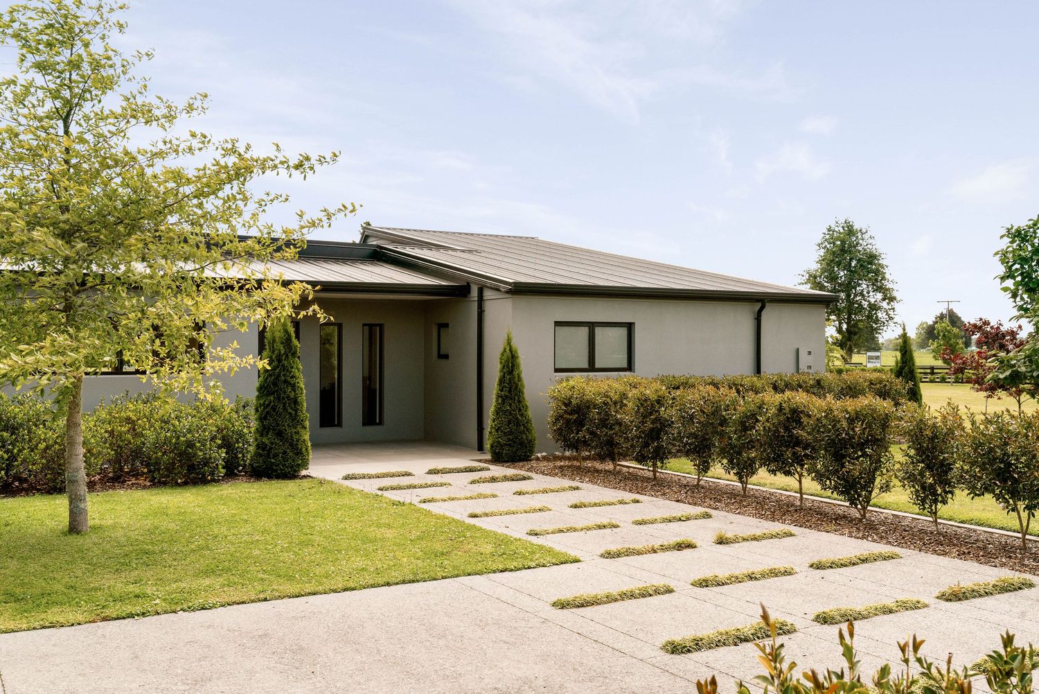 Long concrete driveway leading to contemporary white house surrounded by green landscaping.