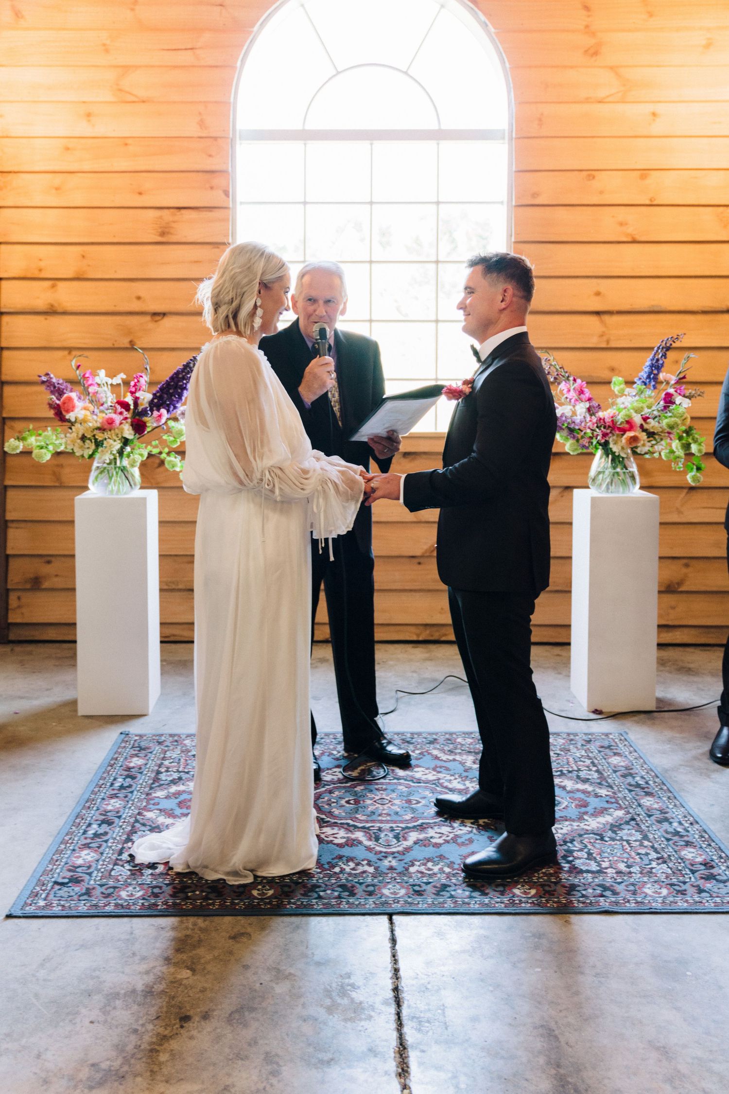 A wedding ceremony in progress inside a rustic wooden chapel with floral arrangements.
