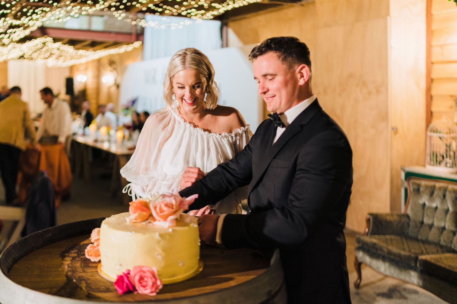 Newlyweds cut their wedding cake together during reception under warm lighting.