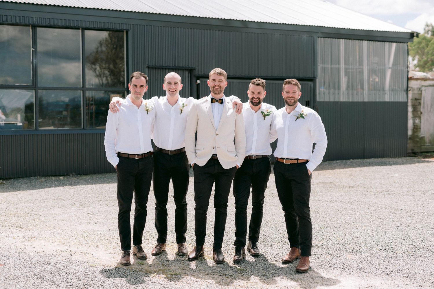 Wedding party members in matching black and white attire pose together outdoors.