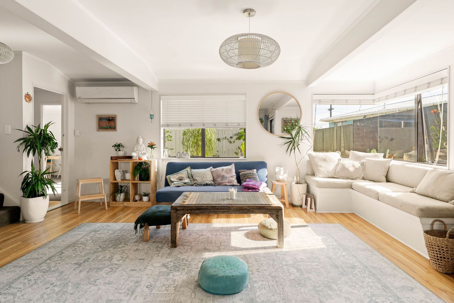 Bright and airy modern living room with white sectional sofa, decorative pillows, plants and circular mirror accent.