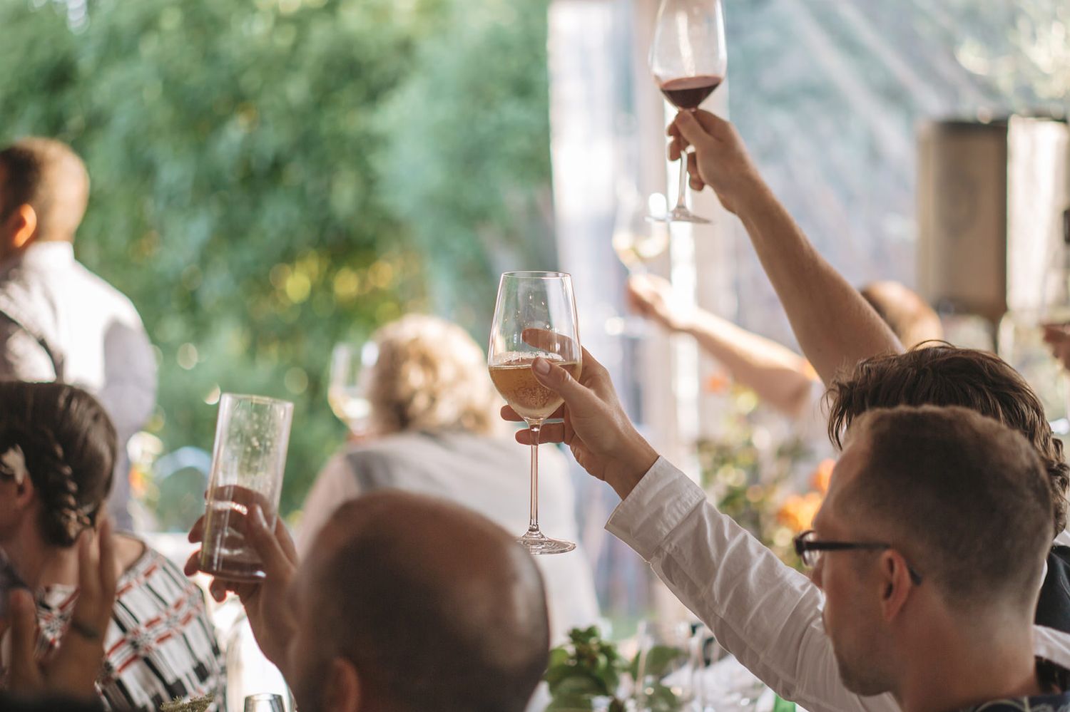 Wedding guests raise their glasses in a celebratory toast during an outdoor reception ceremony.