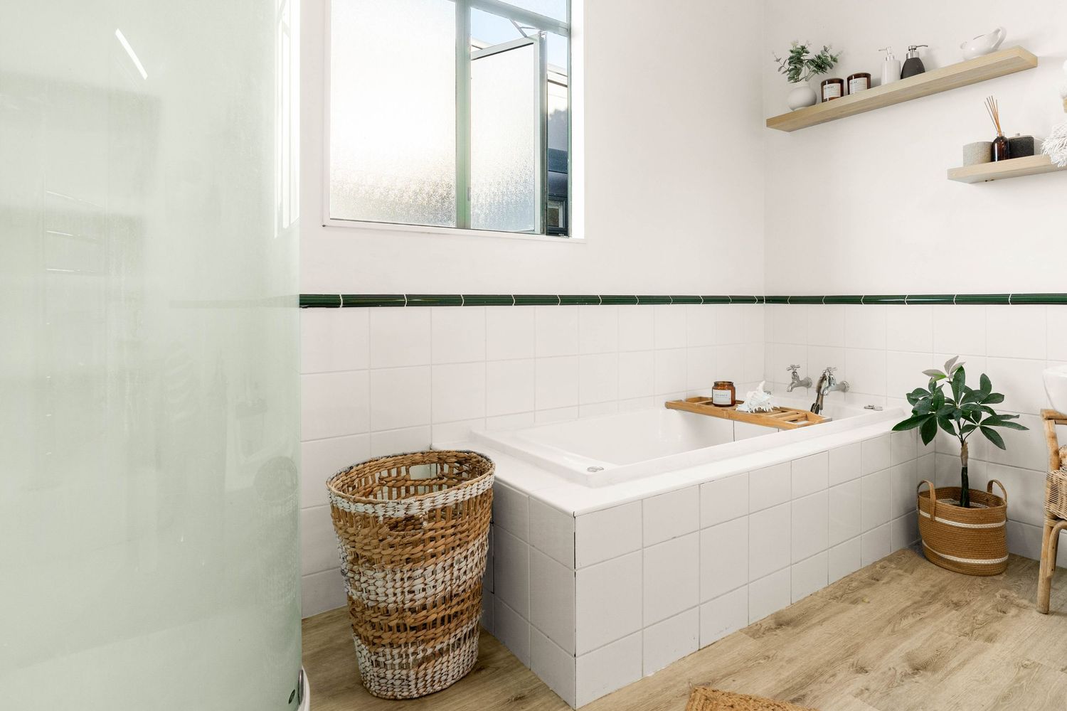 Modern bathroom with white tile, wooden flooring, and woven laundry basket beside built-in bathtub.