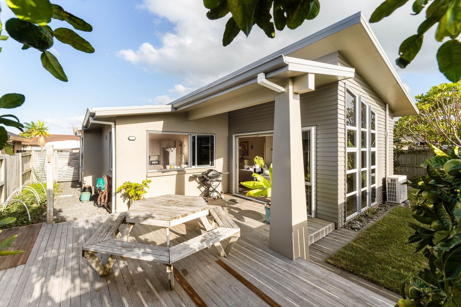 Modern gray beach house with wooden deck and outdoor furniture features angled windows and tropical landscaping.