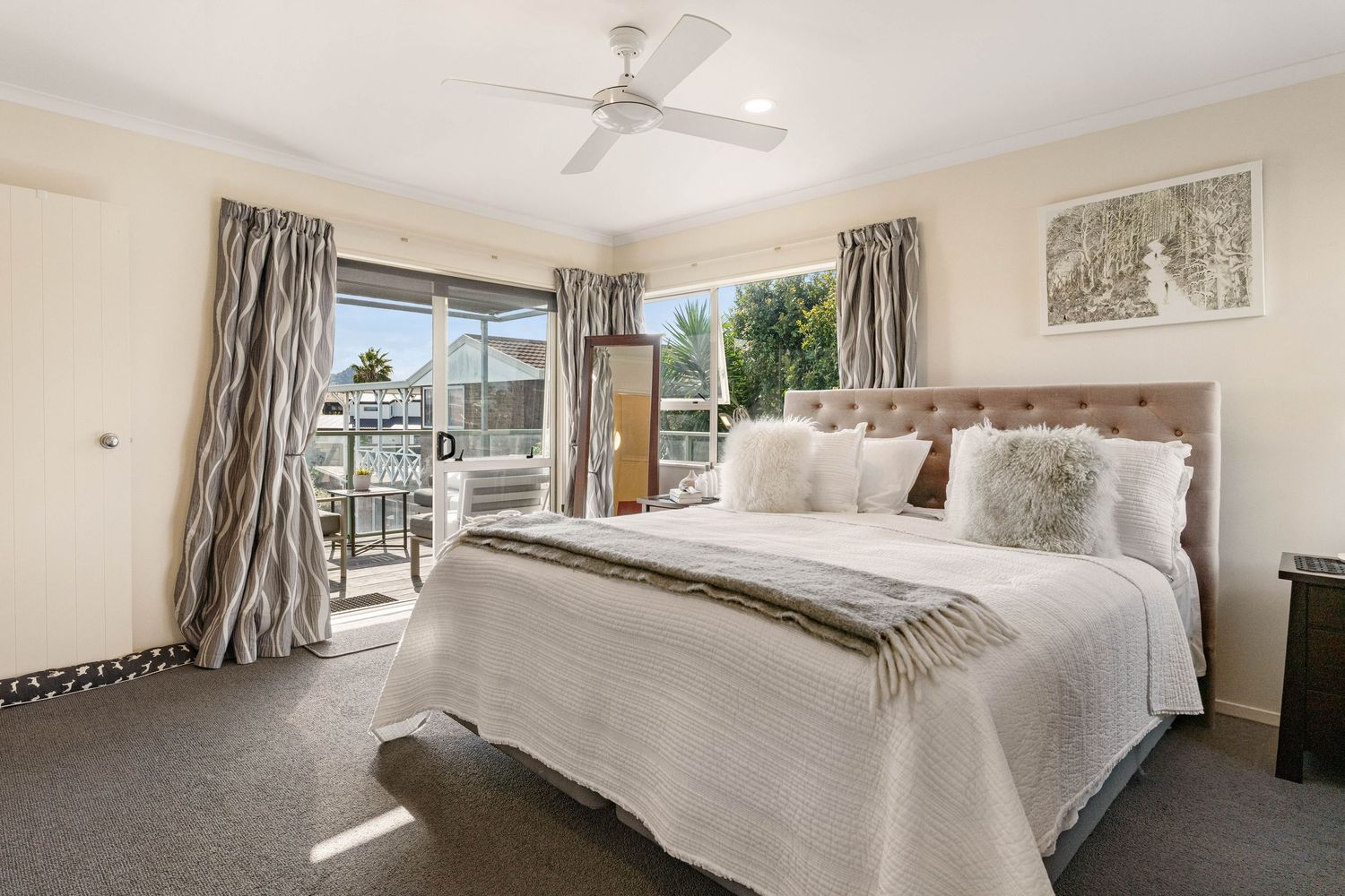 Modern master bedroom with white bedding, patterned curtains and sliding glass doors leading to an outdoor patio.