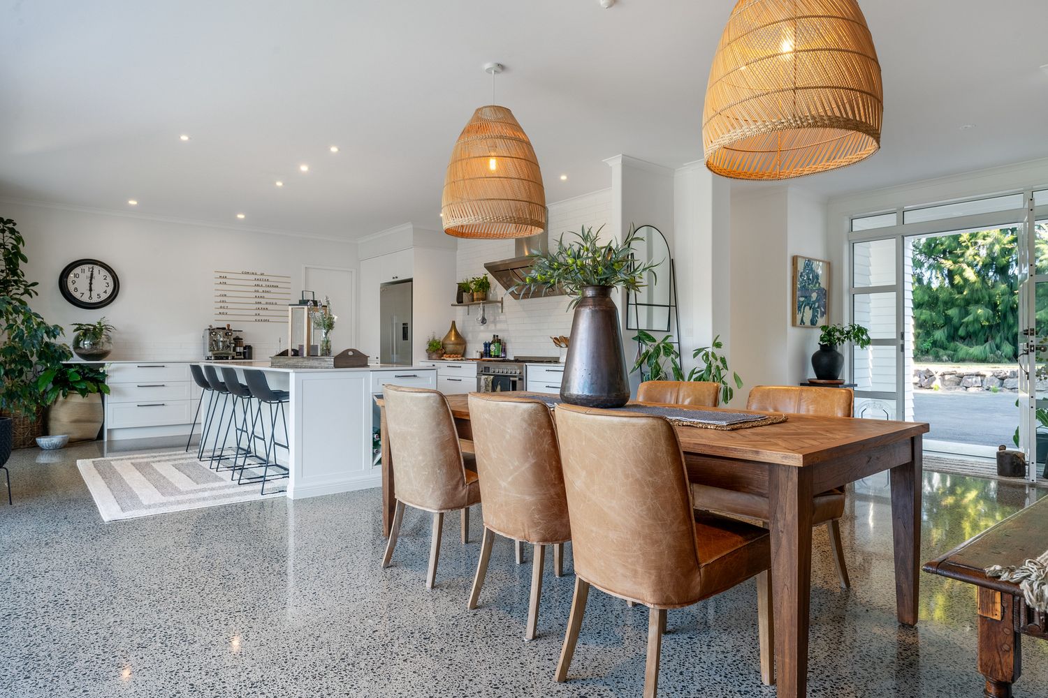 Modern open concept kitchen and dining area with rattan pendant lights and brown upholstered chairs.